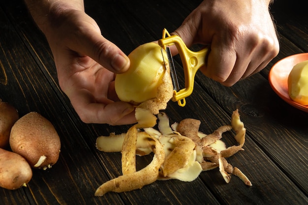 Closeup cook hands are peeling raw potatoes with a potato peeler for preparing a national dish or French fries Delicious vegetable breakfast or lunch