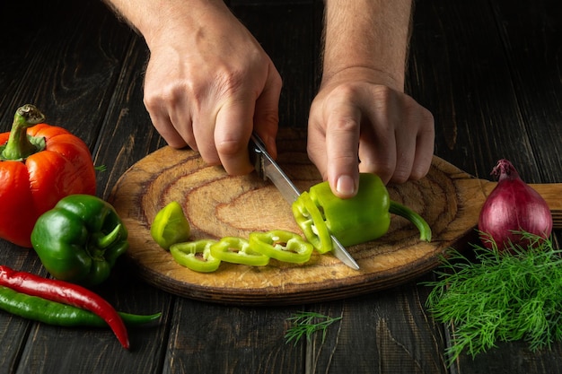 Closeup of the cook hands with knife cut fresh pepper on the cutting board of the restaurant kitchen