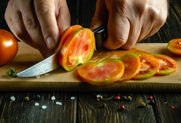 Closeup of a cooks hands with a knife cutting a tomato into small pieces for a vegetable dish for lunch Work environment on the kitchen table