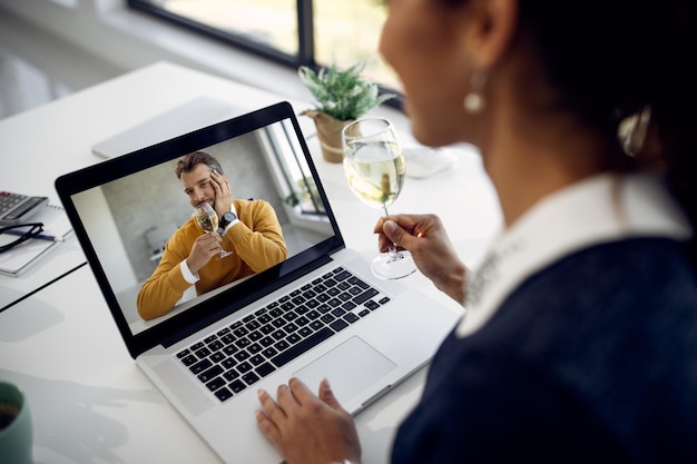 Closeup of couple drinking wine while having online date over a laptop