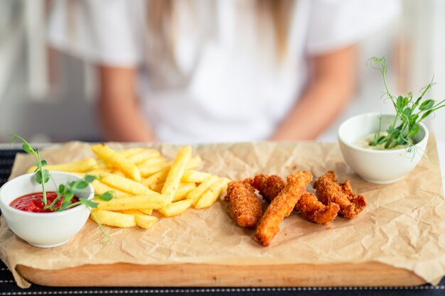 Photo closeup crispy potato fries with two dipping sauce and fresh chicken fingers served on rustic wooden plate