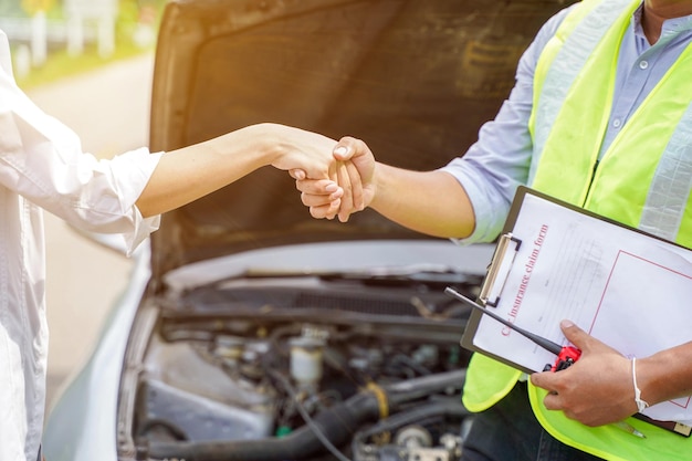 Closeup and crop of a congratulatory handshake of insurance employee and customer with sun flare on car engine background