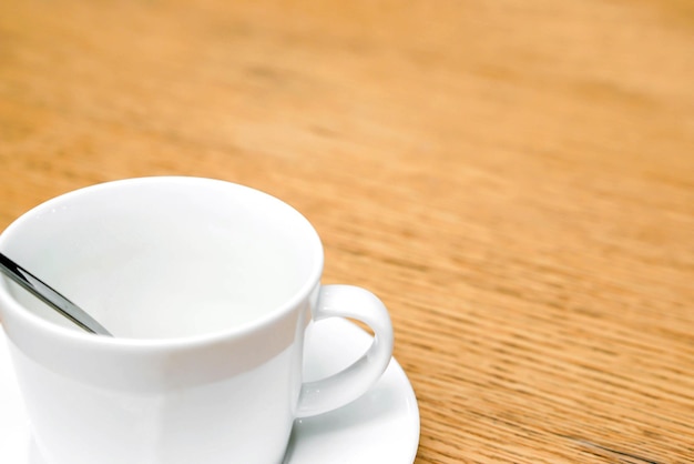 Closeup and crop white coffee cup and spoon with saucer on wooden table