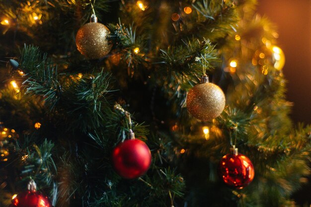 Closeup cropped shot of beautiful Christmas tree decorated with festive balls and celebration warm lights at home selective focus