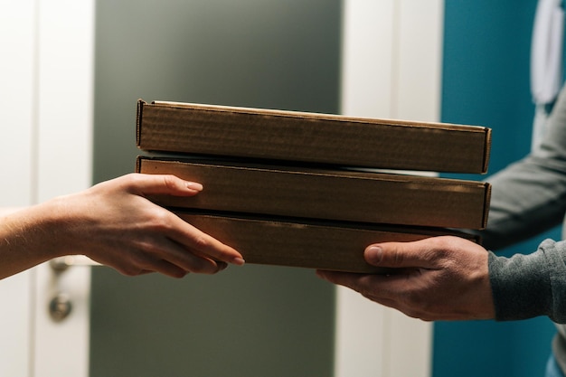 Closeup cropped shot of female customer receiving carton boxes with takeaway at home from delivery man hands