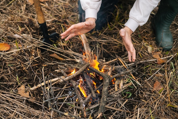 Closeup cropped shot of unrecognizable frozen tourist man warming hands over fire at outdoors on overcast cold day