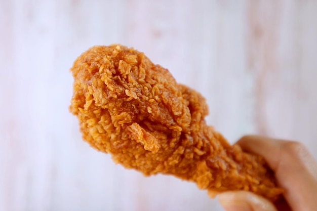 Closeup a Crunchy Fried Chicken Drumstick in Hand with Blurry Wooden Wall in Background