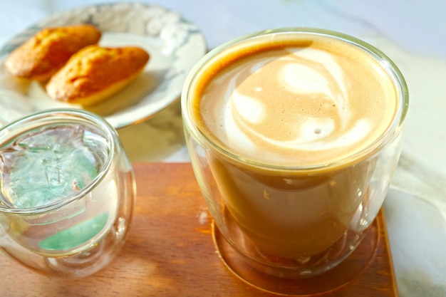 Closeup a Cup of Caffe Latte with Blurry Madeleine Cakes in Backdrop