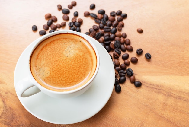 Closeup of a cup of coffee with golden foam and blend coffee beans in a brown sack on wooden table