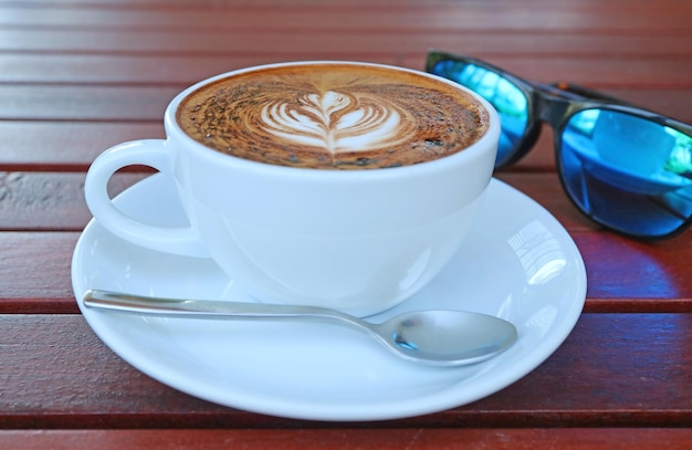 Closeup a Cup of Hot Cappuccino Coffee with Blurry Sunglasses in Background