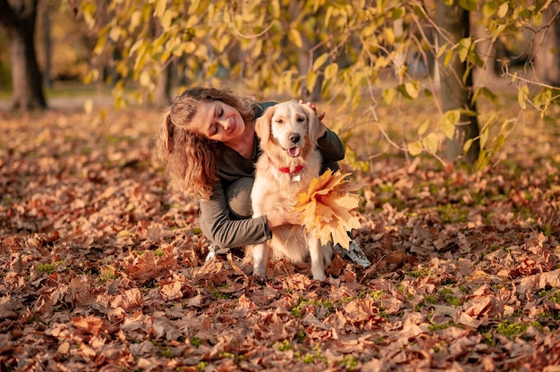 Closeup of curly woman sitting with her dog in autumn leaves outdoors