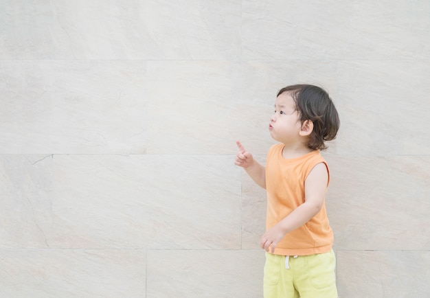 Closeup cute asian kid point to copy space of picture on marble stone wall textured background