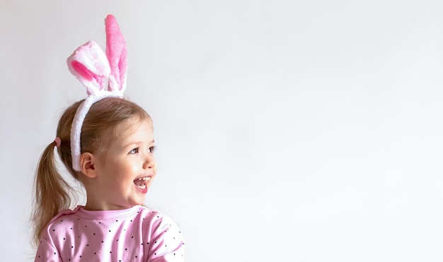 Closeup cute smiling happy girl in a pink shirt with the Easter bunny ears on white background