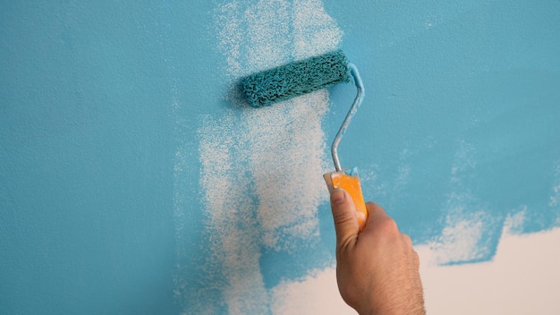 Closeup of decorator hand painting walls in blue color with roller interior decorating repair