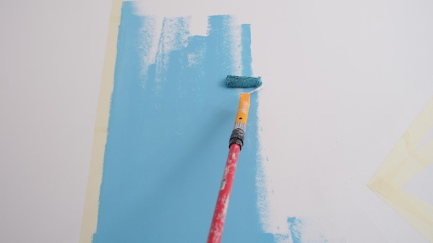 Closeup of decorator painting walls in light blue color with roller interior decorating or