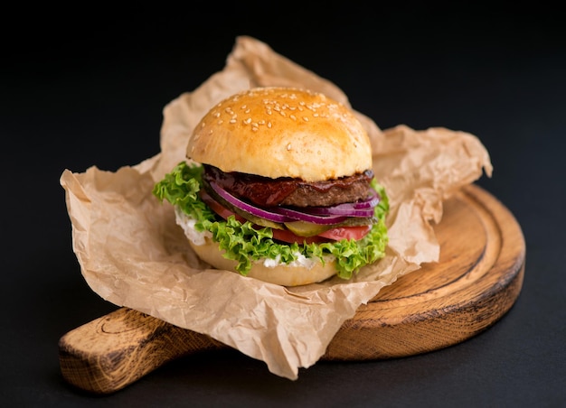 Closeup of a delicious fresh homemade burger with lettuce cheese onion and tomato on a rustic wooden board on a dark background