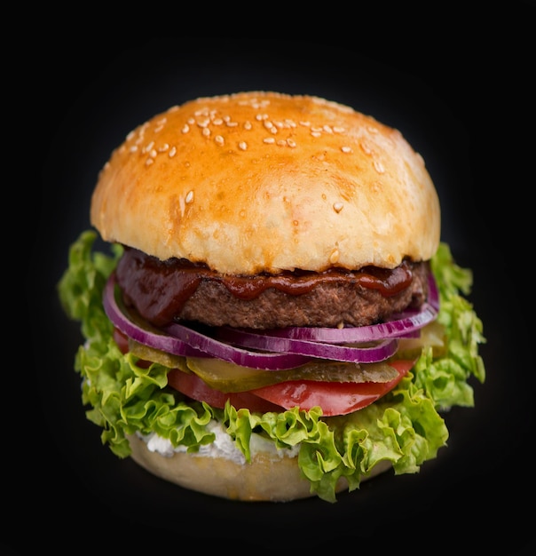 Closeup of a delicious fresh homemade burger with lettuce cheese onion and tomato on a rustic wooden board on a dark background