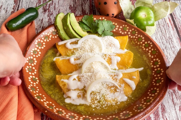 Closeup of delicious Mexican green enchiladas with sour cream and cheese, in a red patterned bowl