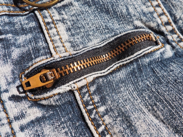 Closeup denim with seams and locks Heavily shabby worn jeans Metal bronze yellow lock with runner Pocket on jeans