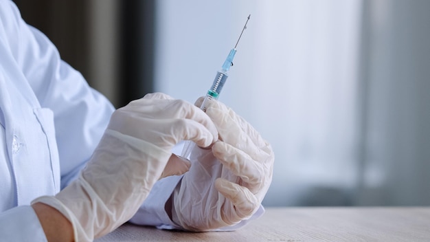 Closeup detail of female hands in latex gloves unrecognizable woman doctor nurse medical worker holding syringe with liquid medicine vaccine antibiotic pandemic remedy sits at table making splashes