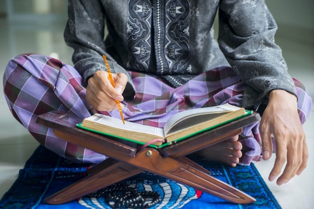 Photo closeup of devout male muslim reading koran on the wooden stand during ramadan time at home