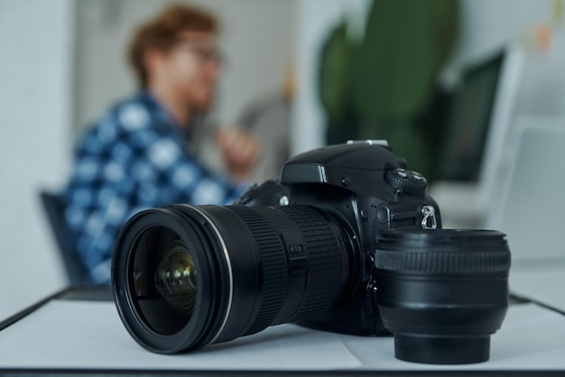 Closeup of digital camera and young man using computer on background