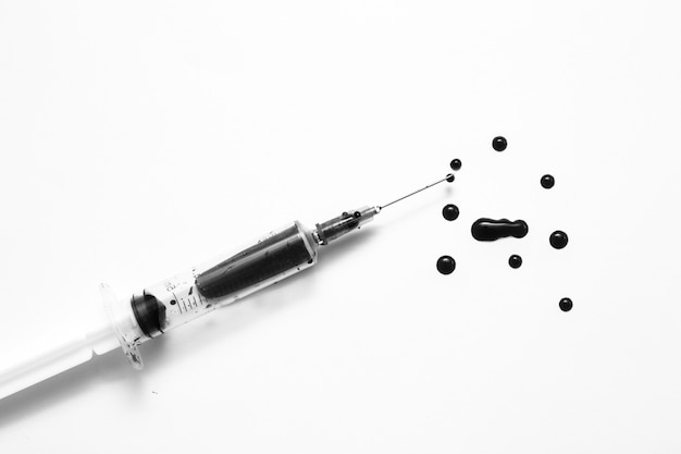 Closeup of a disposable syringe and many blood drops isolated on white black and white