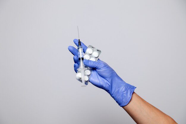 Closeup doctor's hand in rubber latex purple glove hold transparent syringe and pills in blister