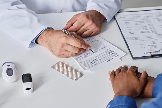 Closeup of doctor writing prescription for patient at table at office