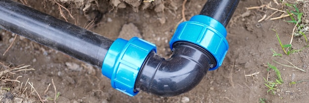 Closeup of elbow fitting and black pvc pipes at bend in trench outdoors plumbing water drainage