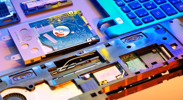 Closeup on electronic motherboard, neon light, hardware repair shop. Blurred panoramic image with opened laptop circuitry, close-up on electronics. Toned background tinted in orange, purple and blue.