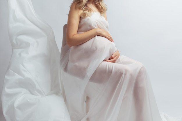 Closeup Elegant pregnant young woman standing wearing flying white fabric Pregnancy maternity and motherhood concept