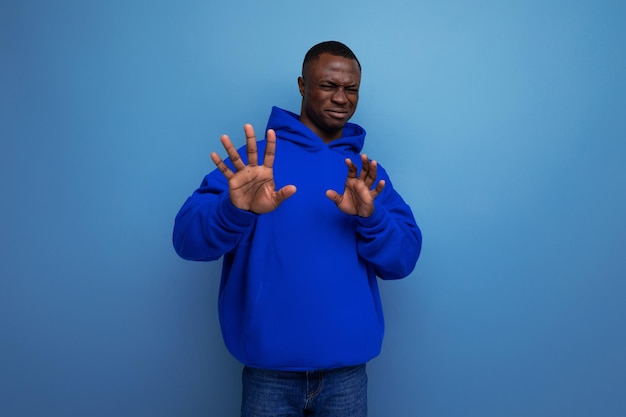 Closeup of an emotional african young guy in a blue sweatshirt with a hood on a studio background