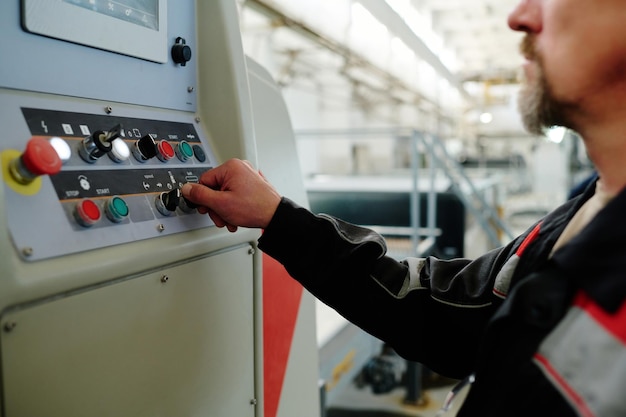 Closeup of engineer in uniform pushing buttons on machine and controlling the work in factory