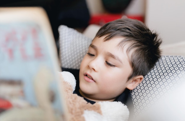 Closeup face School kid reading a book for homeworkHead shot Young boy lying on sofa enjoy reading the story in living roomChild relaxing at home on sunny day SpringHome SchoolingEducation concept