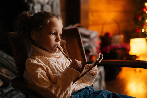 Closeup face of serious thinking little blonde curly child girl writing letter to santa claus