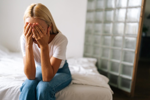 Closeup face of unhappy young woman hiding face in hands feeling desperate cheated hopeless sitting alone at home Upset millennial female crying