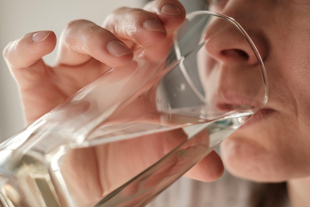 Closeup face of a woman drinking fresh clear water from a glass Health concept