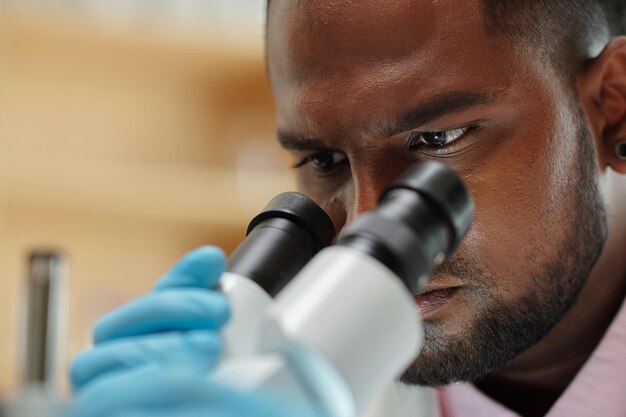 Closeup of face of young scientist or researcher looking in microscope during scientific investigati