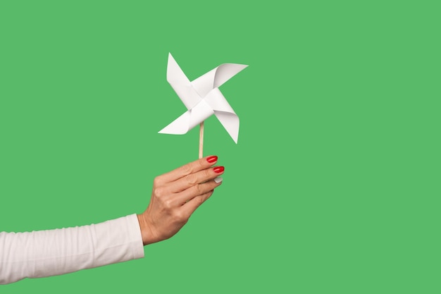 Closeup of female arm holding pinwheel toy on stick origami hand mill isolated on green background