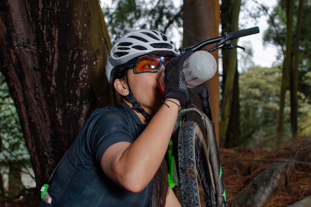 Closeup of a female cyclist sitting in the middle of a forest while hydrating and resting