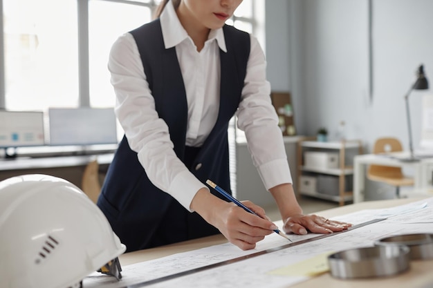 Closeup of female engineer drawing blueprints and plans at workstation in office copy space