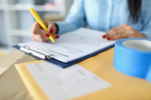 Closeup of female filling information in delivery receipt document clipboard with paper on