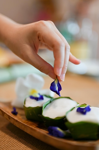 Closeup Female hand garnish her Asian Thai pudding with coconut topping with butterfly pea flower