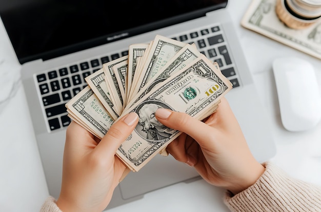 Photo closeup of female hand holding dollar banknotes in front of laptop online earning concept