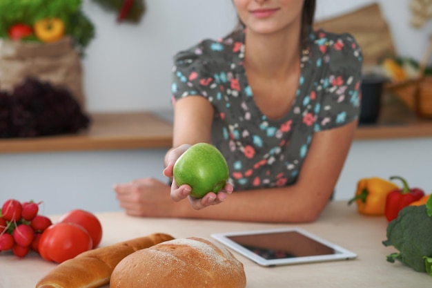 Closeup of female hand holding green apple in kitchen interiors Many vegetables and other meal at glass table are ready for been cooked soon