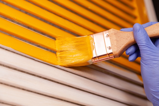 Closeup female hand in purple rubber glove with paintbrush painting natural wooden door with orange paint.  colored bright creative design interior. How to Paint Wooden Surface. Selected focus