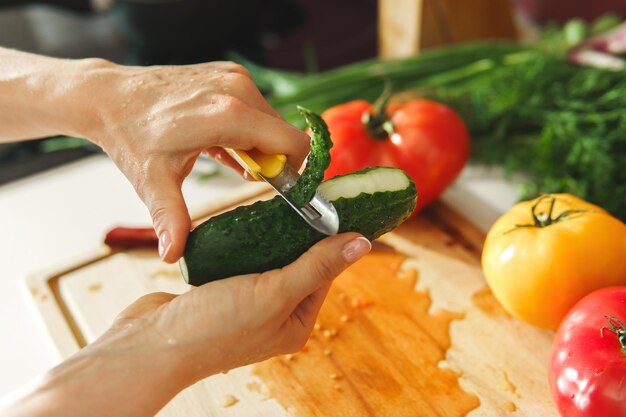 Photo closeup of female hand with peeler and cucumber