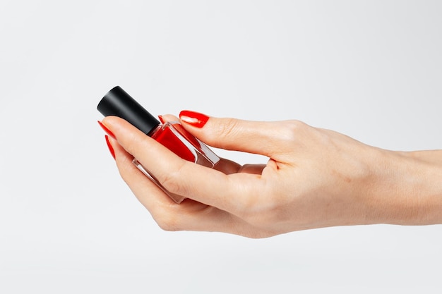 Closeup of female hand with red manicure holding a glitter nail polish of red color on white background