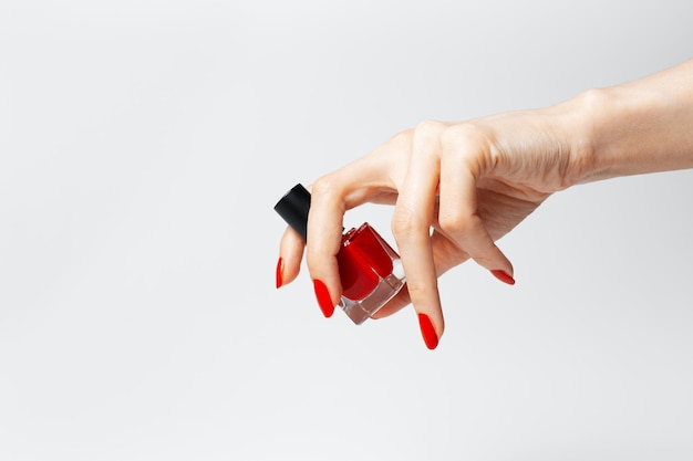 Closeup of female hand with red manicure holding a glitter nail polish of red color on white background